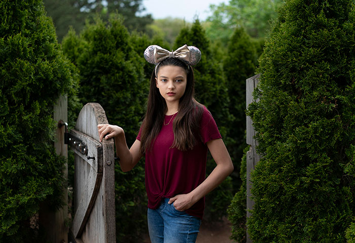 Ashleigh, a young girl with Disney mouse ears standing next to a fencenext to a fence w