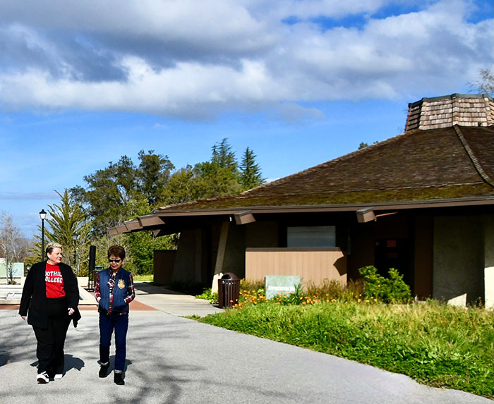 two women walking with wooden building and trees in background