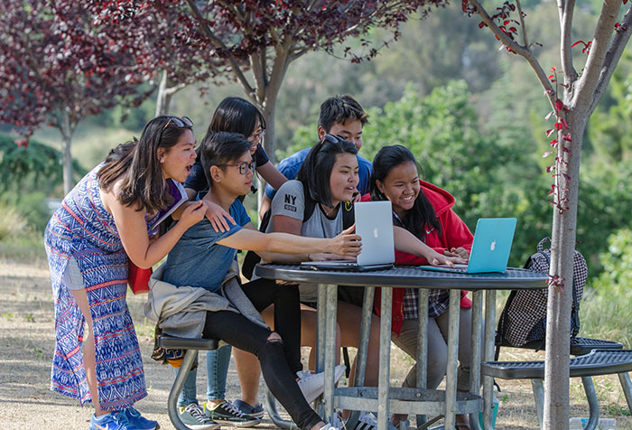 large group of students looking at two laptop screens together